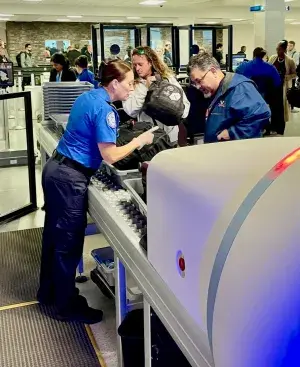 A TSA officer offers some guidance to a traveler as he divests his carry-on items before they go through the computed tomography scanner at Syracuse Hancock International Airport. (TSA photo)