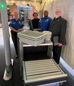A pair of furry friends and their partner stroll through this walk-through metal detector. TSA Officers Denise Childs (left) and Brian Bender provide the screening. (Photo by Albert Stallcup)