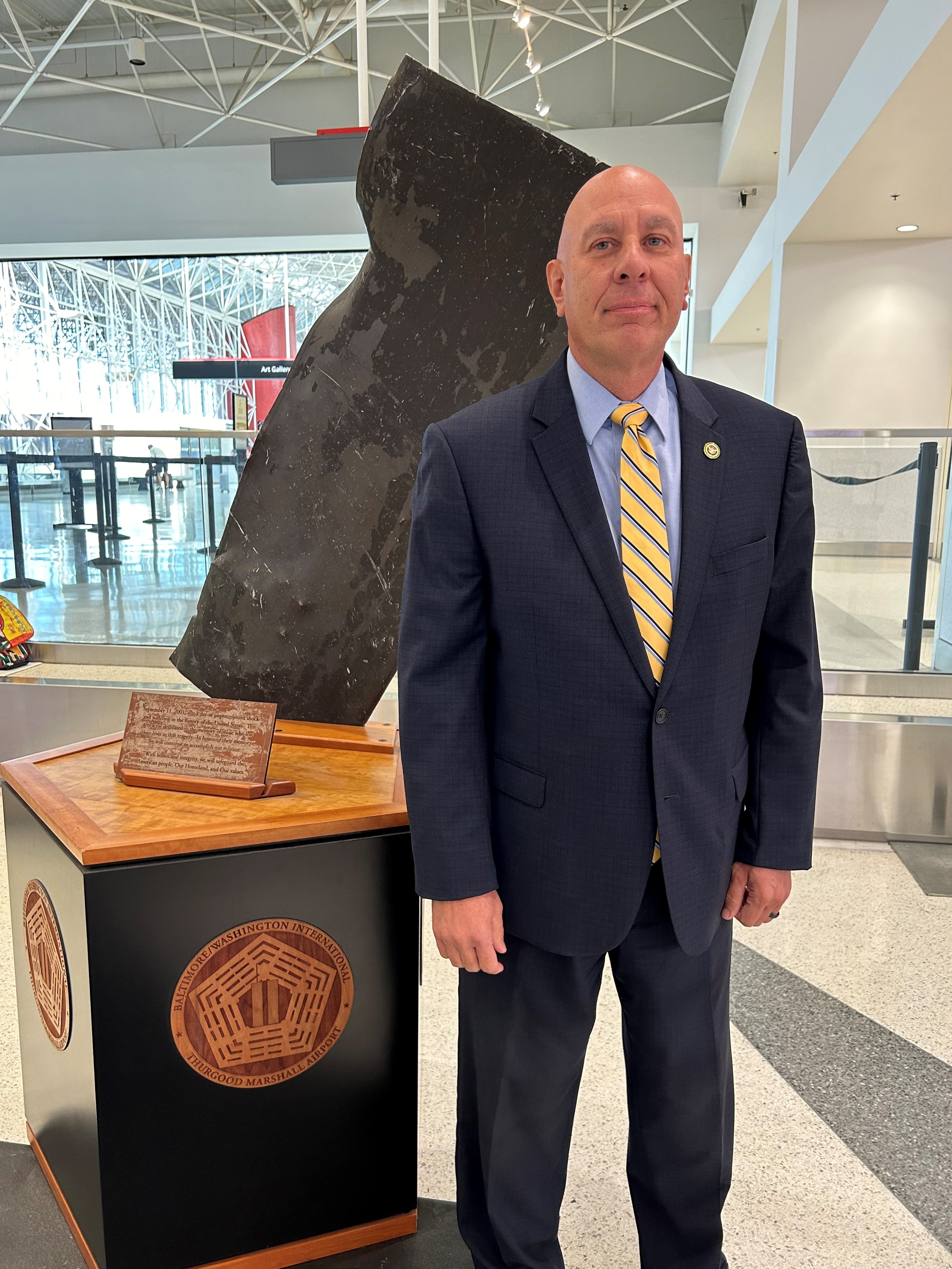 Thomas Battillo stands next to an artifact from the World Trade Center at the Concourse D/E security checkpoint at BWI Airport. (TSA photo)